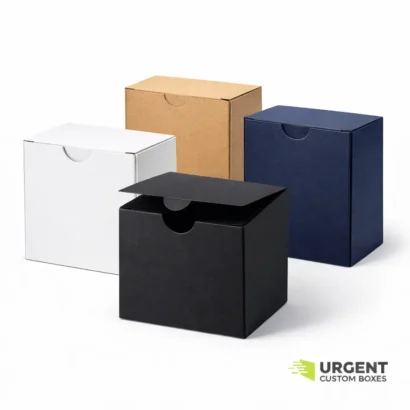 Four tuck top tab lock boxes in white, kraft, black, and navy blue on a white background with Urgent Custom Boxes logo