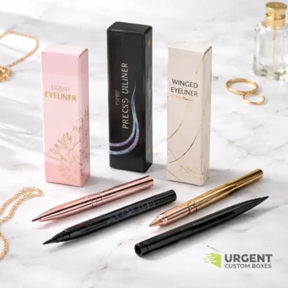 Custom eyeliner boxes with pens on white marble surface, featuring Urgent Custom Boxes logo.