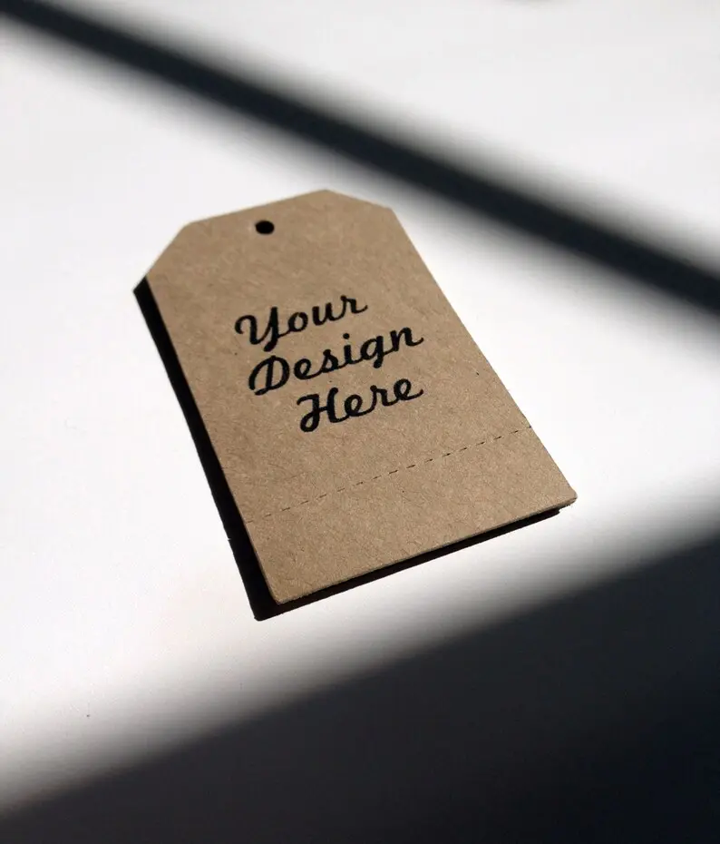 Professional kraft paper hang tag mockup on a minimalist white surface with soft diagonal shadows